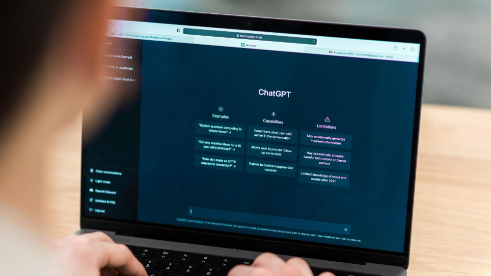 A person using a laptop with the ChatGPT interface open on the screen, displaying examples, capabilities, and limitations of the AI tool.